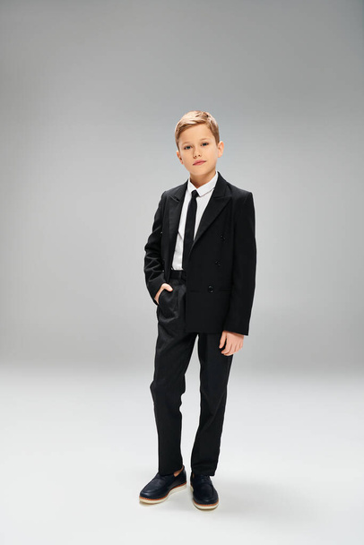 Předpubertální chlapec v obleku a kravatě, stojící na šedém pozadí. - Fotografie, Obrázek