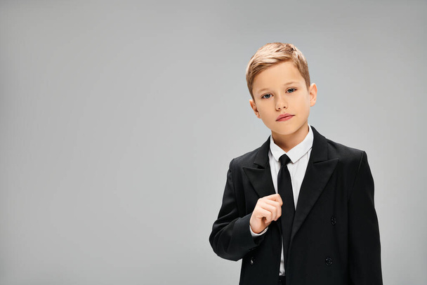 Adorable preadolescent boy in elegant suit and tie against gray backdrop. - Photo, Image