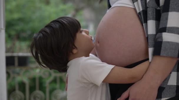 Lindo niño pequeño abrazando el vientre embarazada de la madre mostrando amor y afecto durante la última etapa del embarazo - Metraje, vídeo