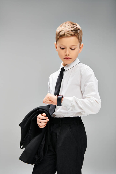 Adorable garçon préadolescent en chemise blanche et cravate noire sur fond gris, exsudant élégance. - Photo, image
