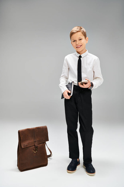 Preadolescent boy stands by briefcase in elegant attire. - Photo, Image
