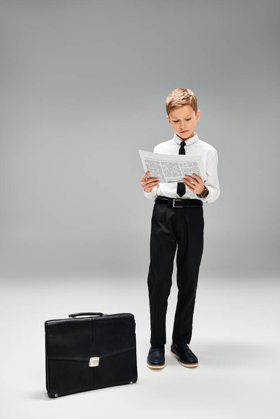 Little boy stands next to suitcase on gray backdrop. - Photo, Image