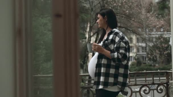 Reflektierende Schwangere auf dem Balkon der Wohnung, warme Getränke in der Hand, Blick auf die Landschaft in der Einsamkeit, Wertschätzung ruhiger Momente im dritten Trimester - Filmmaterial, Video