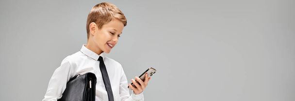 Niño con camisa blanca y corbata, sosteniendo con confianza un teléfono celular. - Foto, imagen