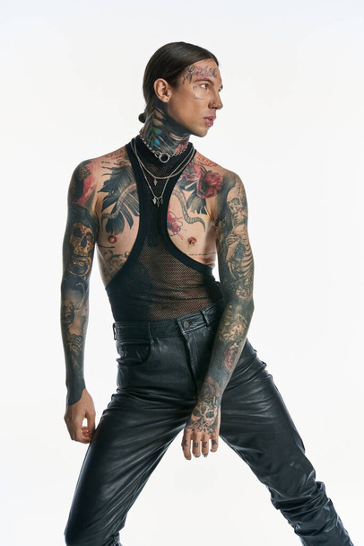 Ένας νεαρός άνδρας επιδεικνύει περίπλοκα τατουάζ και διάφορα σκουλαρίκια στο στήθος του, αποπνέοντας μια αίσθηση αυτοέκφρασης και καλλιτεχνίας.. - Φωτογραφία, εικόνα