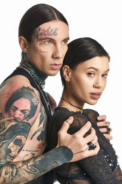 Egy fiatal férfi és nő elegáns tetoválásokkal a karján magabiztosan pózol egy stúdióban, szürke háttérrel.. - Fotó, kép