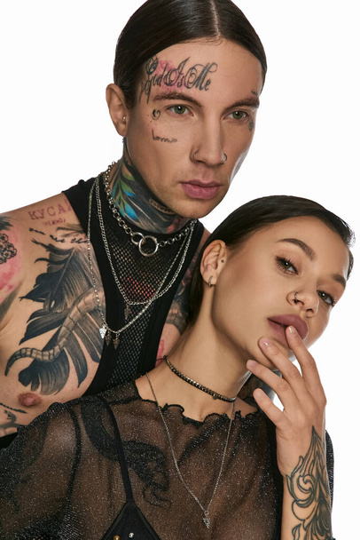 Ein junger Mann und eine junge Frau mit aufwändigen Tätowierungen im Gesicht posieren in einem Studio vor grauem Hintergrund. - Foto, Bild