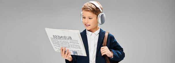 Fiatal fiú elegáns öltözékben, fülhallgatót visel, belefeledkezve az újságok olvasásába.. - Fotó, kép