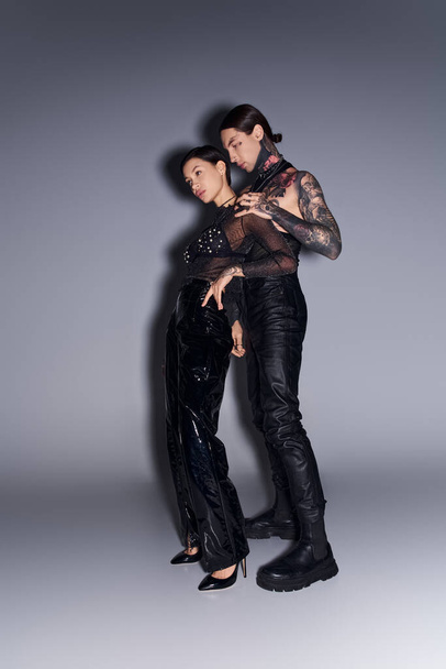 A young tattooed couple posing gracefully in a studio against a grey background. - Photo, Image