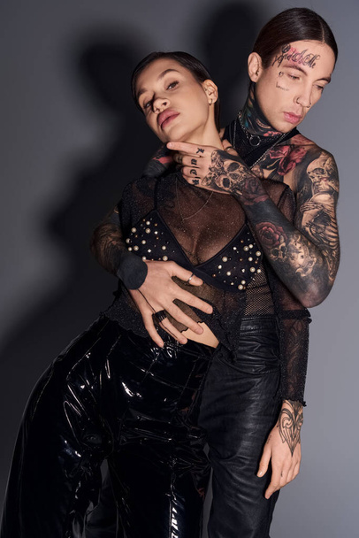 Un jeune couple tatoué se tient côte à côte dans un studio, mettant en valeur leur lien unique et leur individualité. - Photo, image