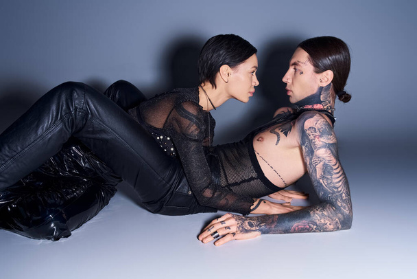 Una giovane coppia tatuata condivide un momento ravvicinato su uno sfondo grigio sereno. - Foto, immagini