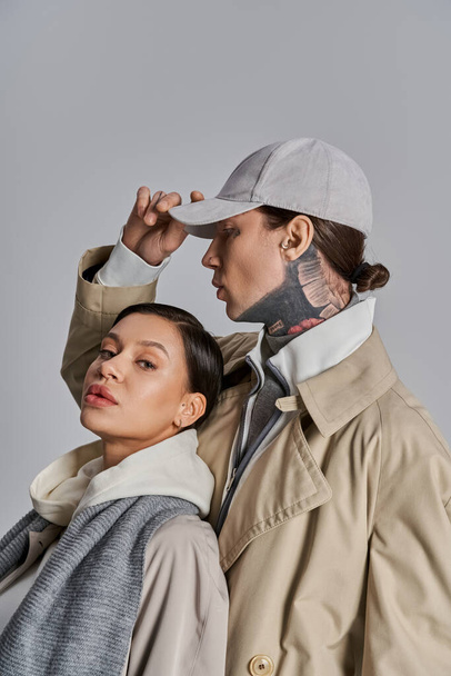 Un jeune homme et une jeune femme vêtus de trench-coats se tiennent côte à côte dans un studio sur fond gris. - Photo, image