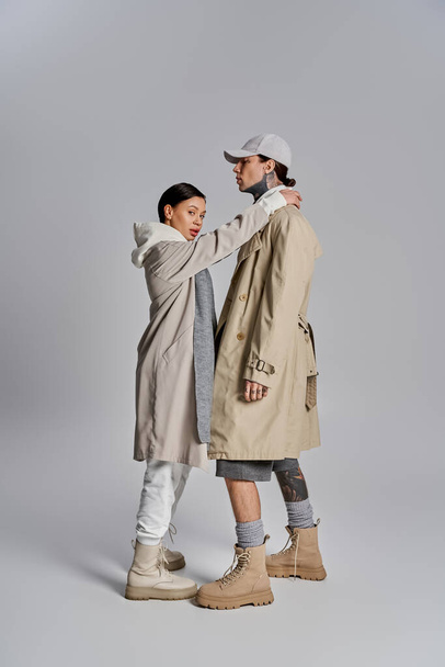 Una pareja joven y elegante en abrigos de trinchera se encuentra elegantemente juntos en un estudio sobre un fondo gris. - Foto, imagen