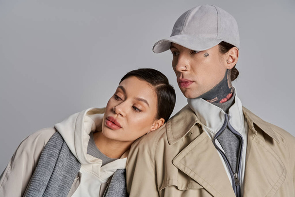 A young stylish couple, dressed in trench coats, are standing closely together in a studio against a grey background. - Photo, Image