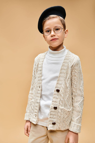 Jonge jongen met bril en hoed, een filmregisseur imiterend, op een beige achtergrond. - Foto, afbeelding