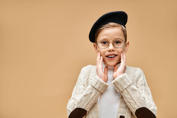 Jeune garçon en lunettes et chapeau, habillé comme un réalisateur, sur fond beige. - Photo, image