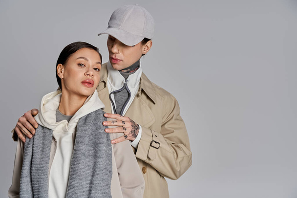 Een jonge man en vrouw, beiden stijlvol gekleed in trench coats, staan zij aan zij in een studio tegen een grijze achtergrond. - Foto, afbeelding