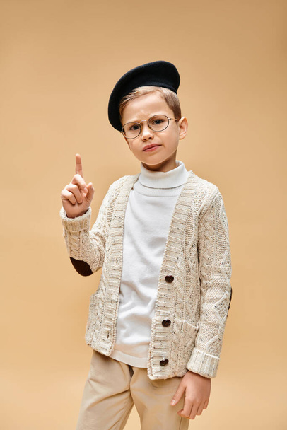 Předdospívající chlapec v brýlích a klobouku oblečený jako filmový režisér na béžovém pozadí. - Fotografie, Obrázek