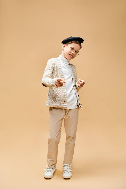 Ένα χαριτωμένο προεφηβικό αγόρι ντυμένο σαν σκηνοθέτης σε μπεζ φόντο.. - Φωτογραφία, εικόνα