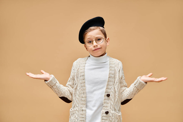 Un lindo niño preadolescente con gafas y sombrero, vestido de director de cine sobre un fondo beige. - Foto, Imagen