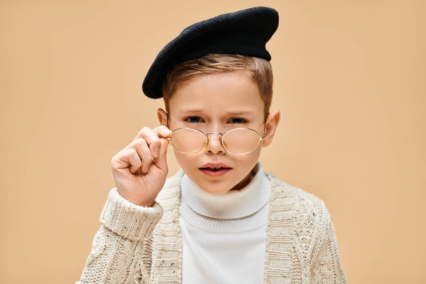 Preadolescent boy in glasses and hat, dressed as a film director on a beige backdrop. - Photo, Image