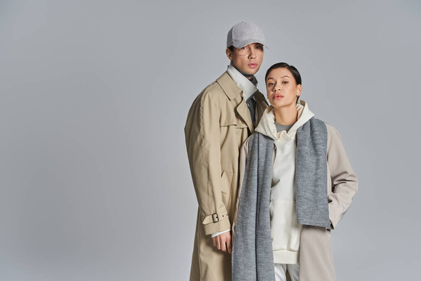 Un jeune couple élégant se tient côte à côte en trench-coat sur fond de studio gris. - Photo, image