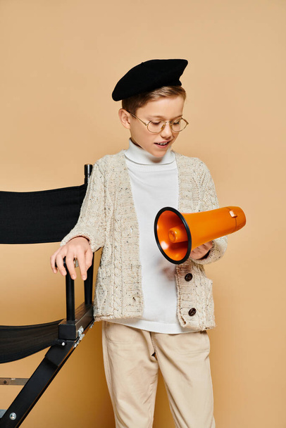 Молодий хлопець, одягнений як кінорежисер, тримає помаранчевий і чорний мегафон. - Фото, зображення