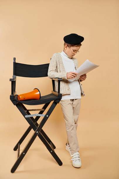 Ragazzo preadolescente vestito da regista cinematografico che legge un articolo sulla sedia pieghevole. - Foto, immagini