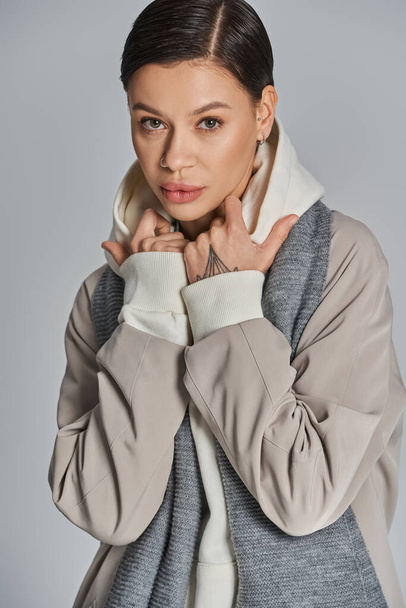 Egy fiatal nő stílust áraszt szürke kabátban és fehér teknős nyak pulóverben egy stúdió szürke hátterében.. - Fotó, kép