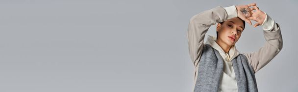 Stylowa młoda kobieta w płaszczu z eleganckim szalikiem owiniętym wokół szyi w studio na szarym tle. - Zdjęcie, obraz
