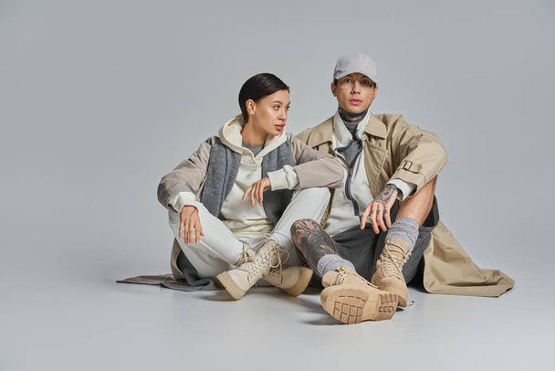 A man and a woman seated on the ground engaged in deep discussion. The woman, in a stylish trench coat, looks attentive. - Photo, Image