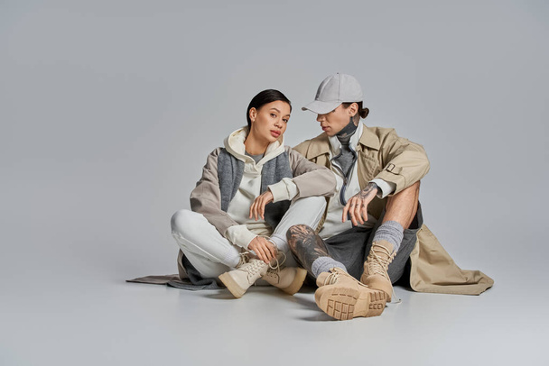 Mężczyzna i kobieta w stylowym stroju siedzą razem na ziemi, zaangażowani w głęboką rozmowę lub moment połączenia. - Zdjęcie, obraz
