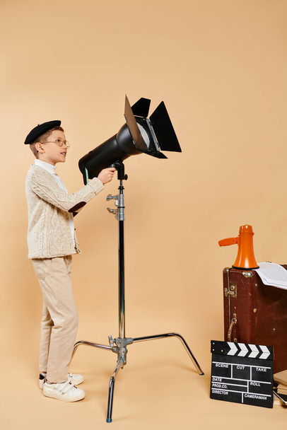Предприимчивый мальчик уверенно стоит рядом с камерой и штативом. - Фото, изображение