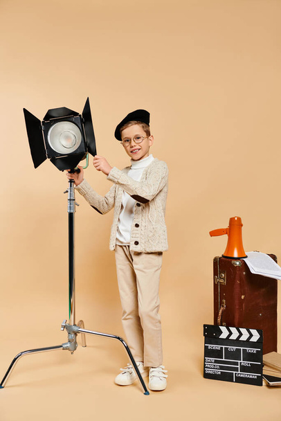Un lindo niño preadolescente vestido como director de cine posa con una luz en la mano sobre un fondo beige. - Foto, imagen