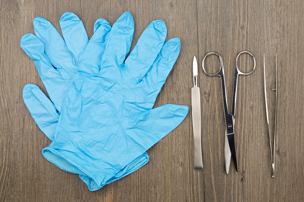 Silver scalpel surgical scissors and forceps beside blue latex glove - Photo, Image
