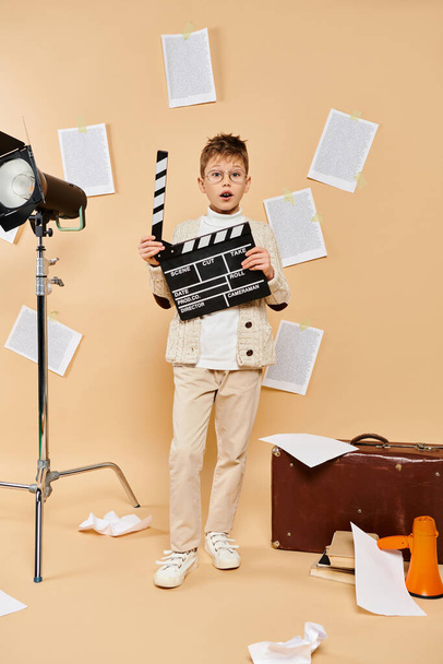 Nastoletni chłopiec w kostiumie reżysera filmowego trzymając łupek przed kamerą. - Zdjęcie, obraz