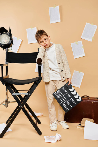 Jonge jongen staat naast stoel, verkleed als filmregisseur. - Foto, afbeelding