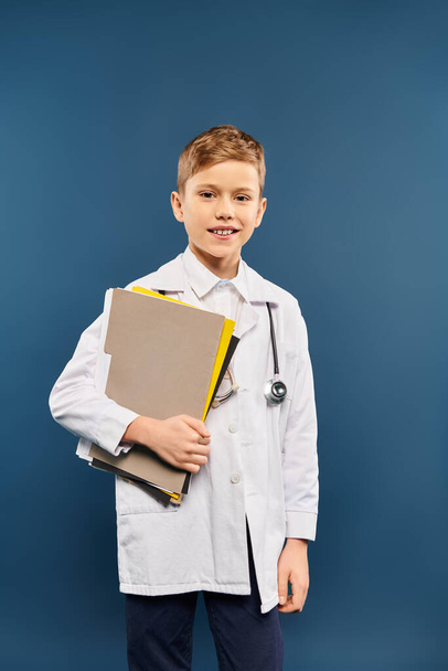 Un niño preadolescente con una bata de laboratorio sostiene un aglutinante, encarnando el papel de un científico. - Foto, Imagen