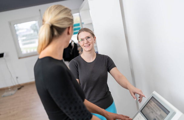Entrenadora femenina que apunta a una pantalla de escalas de composición corporal para explicar a su cliente la función de una prueba Inbody en un gimnasio - Foto, imagen