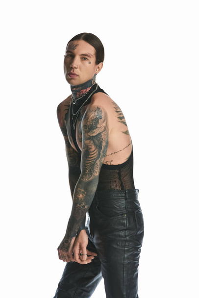 Een stijlvolle jongeman toont trots een tatoeage op zijn arm in een studio tegen een grijze achtergrond. - Foto, afbeelding