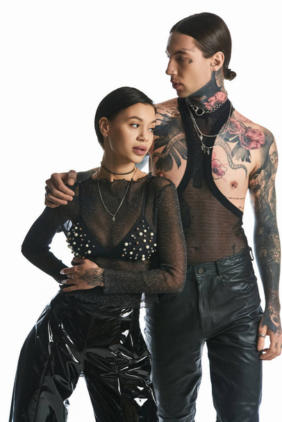 Egy stílusos, tetovált férfi és nő áll egymás mellett egy stúdióban, szürke háttérrel, bemutatva egyedi megjelenésüket.. - Fotó, kép