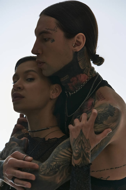Casal jovem e elegante com tatuagens no braço, posando em um estúdio contra um fundo cinza. - Foto, Imagem