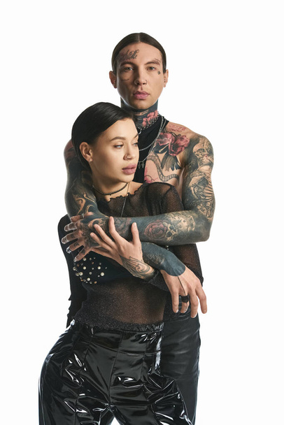 Ένα νεαρό, κομψό ζευγάρι με περίπλοκα τατουάζ στα χέρια ποζάρει σε ένα στούντιο με γκρι φόντο.. - Φωτογραφία, εικόνα