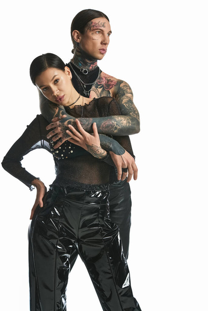 Ένα νεαρό, κομψό ζευγάρι με τατουάζ ντυμένο με λατέξ ρούχα ποζάρει σε ένα στούντιο πάνω σε γκρι φόντο.. - Φωτογραφία, εικόνα