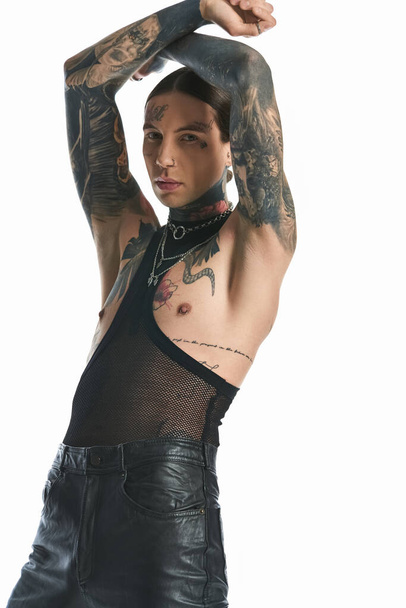 Un jeune homme tatoué au bras et à la poitrine pose dans un studio sur fond gris. - Photo, image