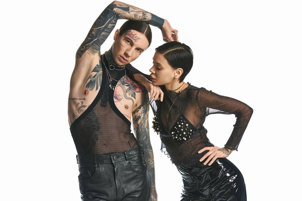Un homme et une femme jeunes, élégants et tatoués posant ensemble dans un studio sur un fond gris. - Photo, image