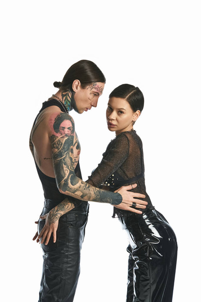 Een stijlvolle jonge man en vrouw versierd met tatoeages staan samen in een studio tegen een grijze achtergrond. - Foto, afbeelding