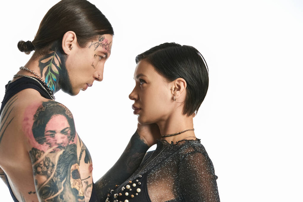 Ένα κομψό νεαρό ζευγάρι με τατουάζ να στέκονται το ένα δίπλα στο άλλο σε ένα στούντιο με γκρι φόντο.. - Φωτογραφία, εικόνα