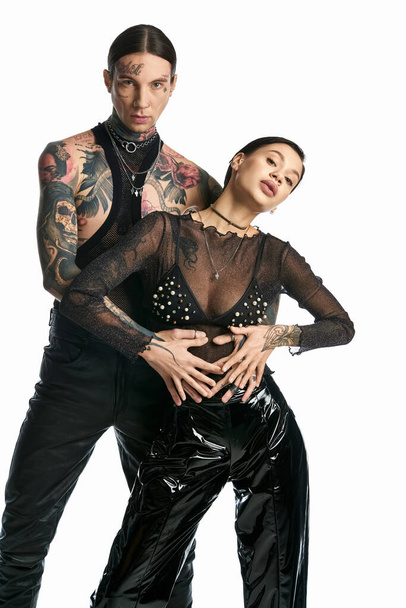 Un joven hombre y una mujer tatuados con trajes negros se unen en una pose elegante sobre un fondo gris de estudio. - Foto, imagen