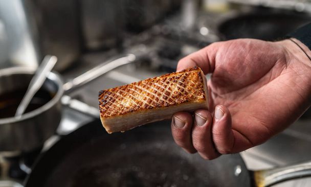 Kézen fogva egy ropogós sertés hasát, amit forró serpenyőben sütöttek egy profi konyhában egy étteremben. Luxus hotel főzés koncepció kép. - Fotó, kép